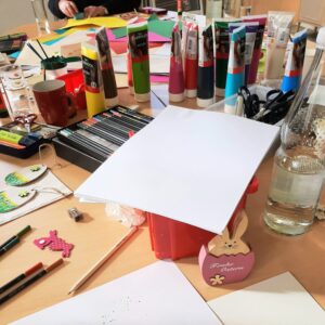 Bastelmaterialien wie Stifte, Acrylfarbe und Papier auf dem Tisch