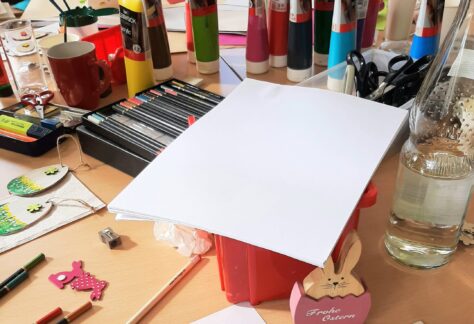 Bastelmaterialien wie Stifte, Acrylfarbe und Papier auf dem Tisch